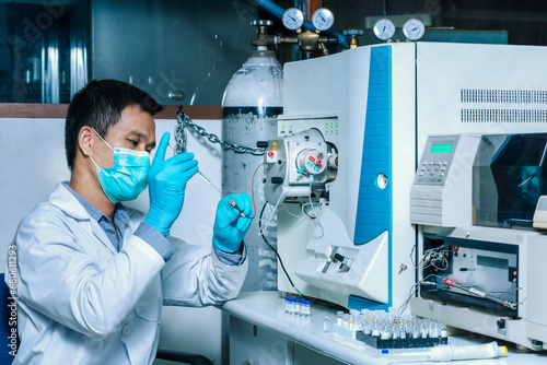 A scientist man injects a sample with a micro syringe into Mass Spectrometer to analyze samples, Mass spectrometry is used to measure mass per charge connected to Liquid Chromatography LC-MS