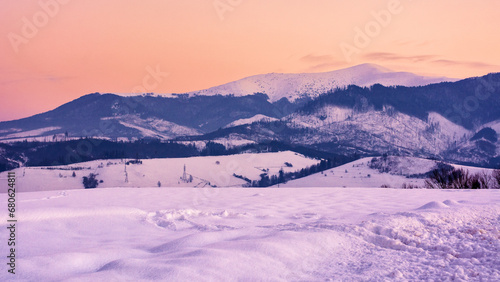 mountainous countryside at sunset. beautiful winter landscape with snow covered hills and meadows in evening light. snow capped tops of borzhava ridge in the distance