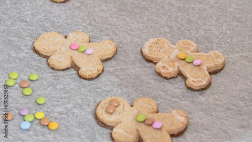 woman's hands decorating a gingerbread man-shaped Christmas cake with white icing and colored caramels, close-up