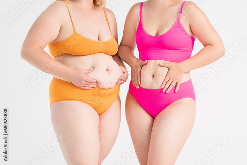 Tummy tuck, two fat women with flabby bellies on gray background, plastic surgery and body positive concept