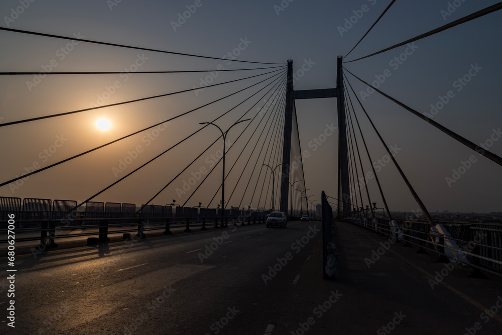 Cable stayed suspension bridge known as the Vidyasagar Setu built on the river Ganges at sunset with view of a boat seen from Princep Ghat at Kolkata, India