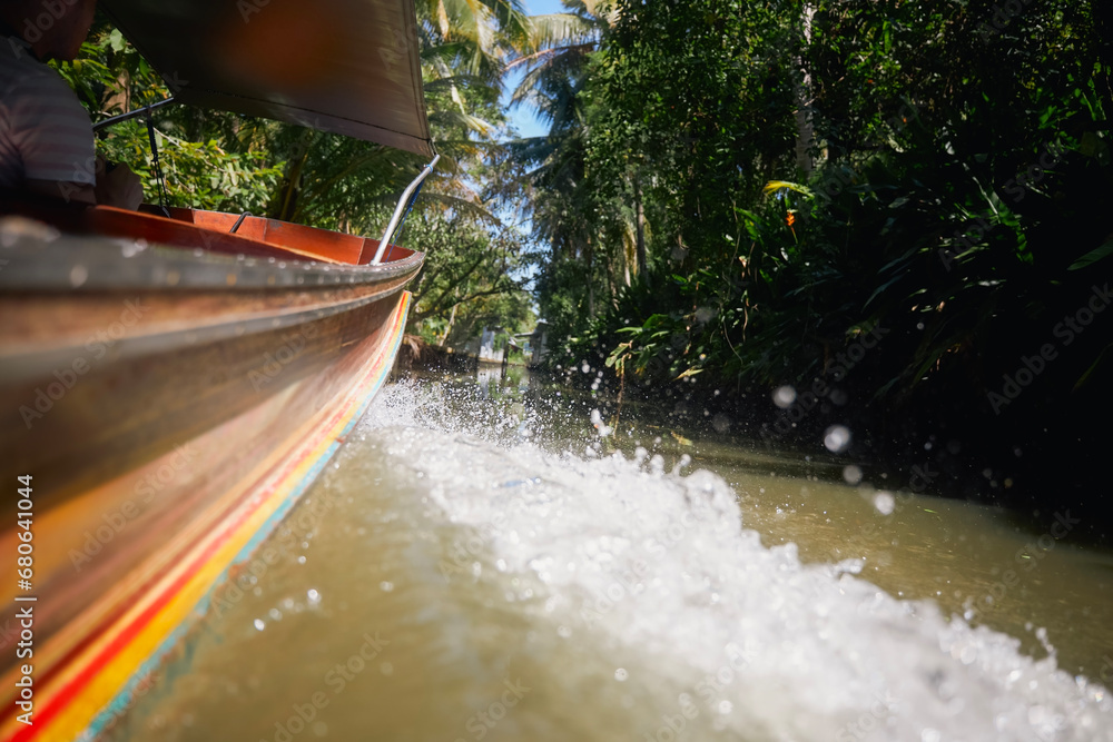 Rippled water and splashing drops behind traditional wooden long tail boat. Speed boat on river canal among palm trees in Thailand. Themes travel and adventure..