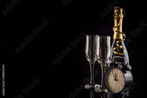 Alarm clock, champagne and glasses on black background with copy space. New Year and Christmas celebration concept.