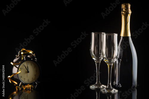 Champagne bottle and two glasses on a black background with a clock. New Year and Christmas celebration concept.