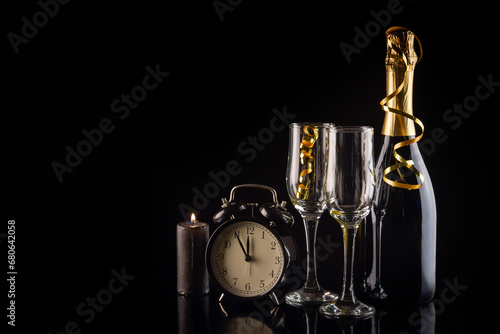 Alarm clock, champagne bottle and glasses on a black background. New Year and Christmas celebration concept.