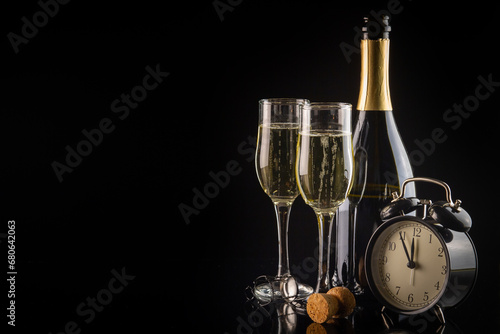 Champagne glasses and alarm clock on black background with copy space. New Year and Christmas celebration concept.