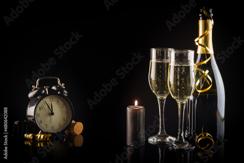 Champagne bottle and two glasses on a black background with a clock. New Year and Christmas celebration concept.