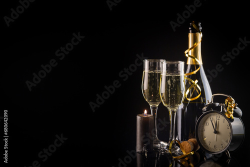 Champagne glasses, alarm clock and candle on black background with copy space. New Year and Christmas celebration concept.