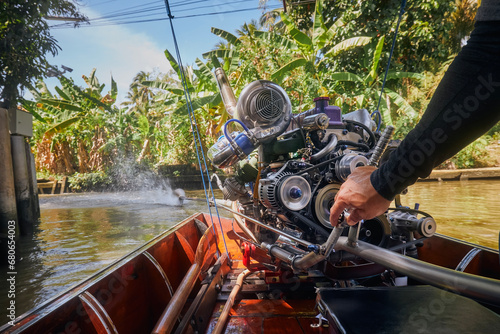 Powerful engine of traditional long tail boat in Thailand. Hand of drive control boat in narrow water canal leading to floating market Damnoen Saduak. . photo