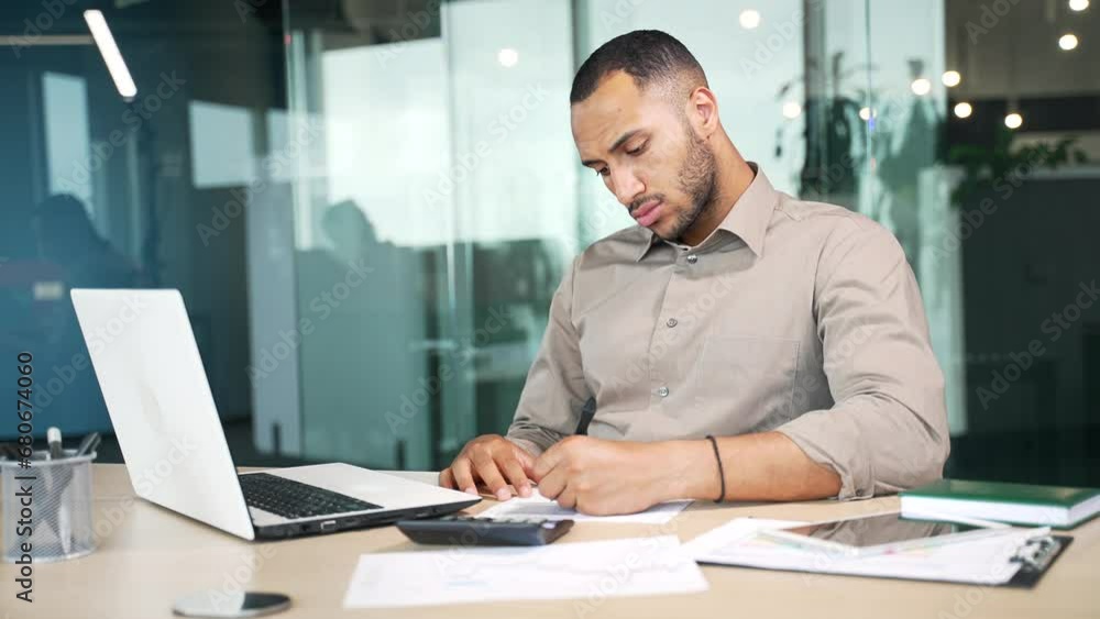 Focused confident business man, employee, accountant booker working at laptop computer. Thoughtful serious male is engaged in accounting and paperwork in a modern glass office sitting at desk. Indoor Focused confident business man, employee, accountant booker working at laptop computer. Thoughtful serious male is engaged in accounting and paperwork in a modern glass office sitting at desk. Indoor