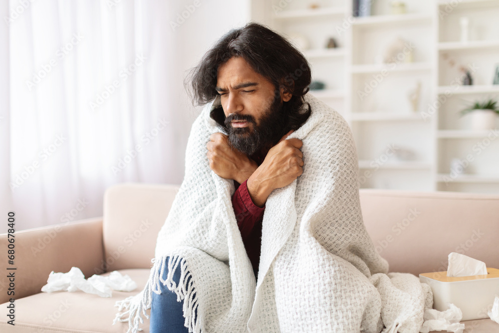 Sick indian guy sitting on couch covered in blanket Sick indian guy sitting on couch covered in blanket