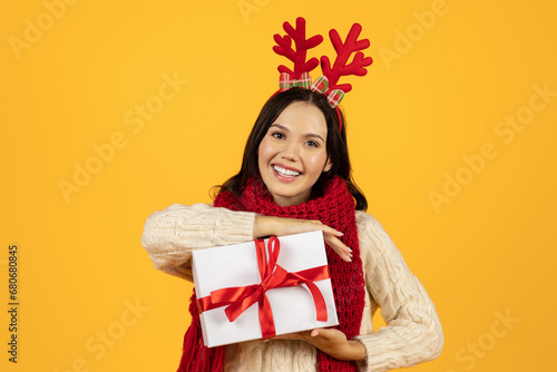 lady holding Christmas gift box posing in festive antlers, studio