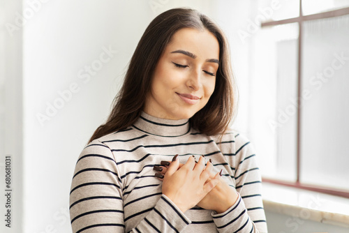 Cheerful calm young arab lady with closed eyes press hands to chest heart, make thanks sign