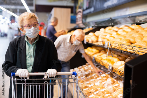 Older woman with glasses chooses buns and bread in supermarket bakery photo