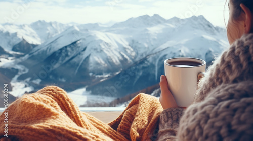 Feet in woolen socks overlooking the mountains through the Alps. A woman relaxes with a mountain view, enjoying a cup of hot drink. Close-up on the feet. The concept of winter holidays and Christmas