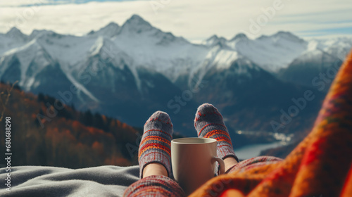 Feet in woolen socks overlooking the mountains through the Alps. A woman relaxes with a mountain view, enjoying a cup of hot drink. Close-up on the feet. The concept of winter holidays and Christmas © Karol