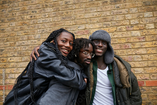 Group of three black friends embracing each other and showing off their unique style in front of brick wall 