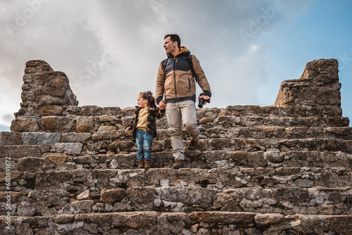 Photographer man and his fashionable little son sightseeing together in a castle walking down stairs hand in hand while looking at the surroundings, traveling and photographing a small town