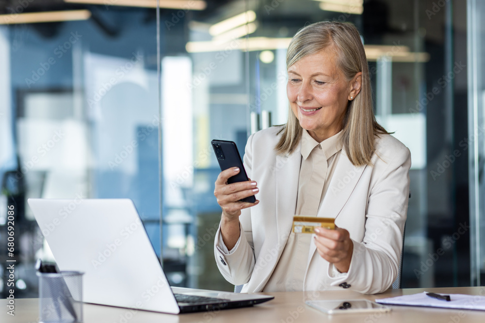 Senior businesswoman working in office at desk, using mobile phone and credit card. Senior businesswoman working in office at desk, using mobile phone and credit card.
