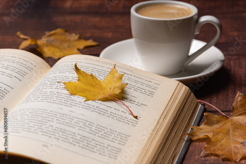 Autumn leaves, cup of coffee and open book on wooden table, autumn reading, cozy home © Marek