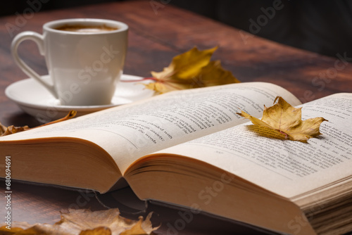 Autumn leaves, cup of coffee and open book on wooden table, autumn reading, cozy home © Marek