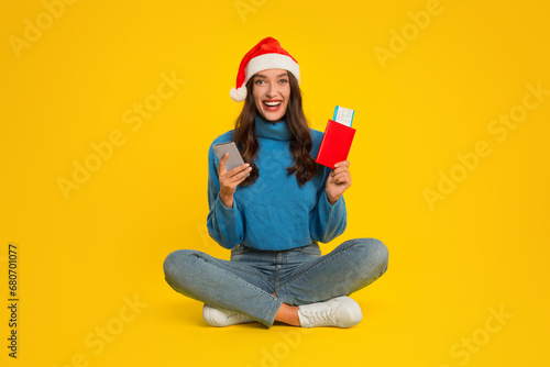 woman in Santa hat holds phone and tickets, yellow background