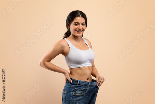 Happy Young Indian Woman Wearing Oversized Jeans Demonstrating Weight Loss Result © Prostock-studio