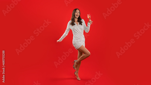 woman in dress cheers with wine glass on red background