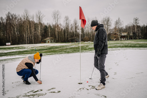 Fotografie Men puttering on a snowy green, golf game.