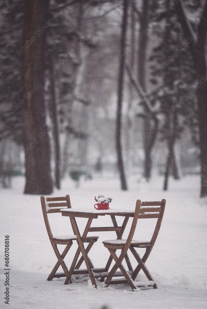 Christmas outdoor terrace with table, chairs and Christmas decorations and lights. a snowy winter street scene. Christmas cafe with wooden table, chairs and Red cup with spruce branches and red berry.