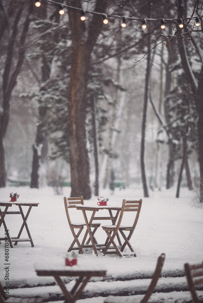 Christmas outdoor terrace with table, chairs and Christmas decorations and lights. a snowy winter street scene. Christmas cafe with wooden table, chairs and Red cup with spruce branches and red berry.