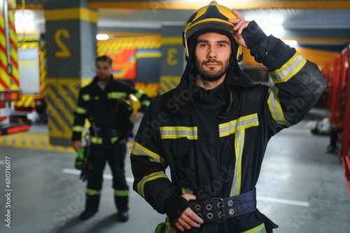 Portrait of two young firemen in uniform standing inside the fire station © Serhii