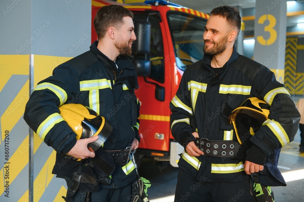 Fototapeta premium Two firefighters in protective clothing in helmets with fire engine