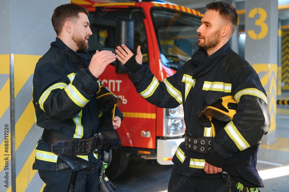 Two firefighters in protective clothing in helmets with fire engine Two firefighters in protective clothing in helmets with fire engine