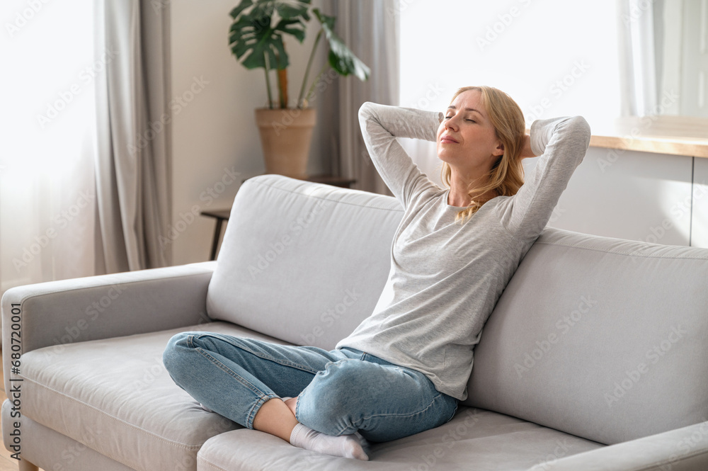 Calm woman sitting on couch and holding hands behind head