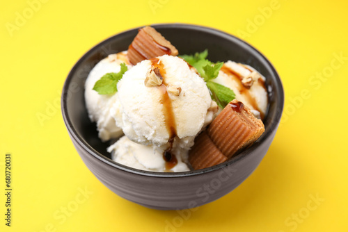 Tasty ice cream with caramel sauce, mint, candies and nuts in bowl on yellow background, closeup