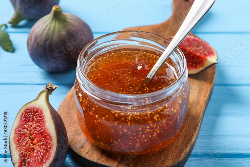 Jar of tasty sweet jam and fresh figs on light blue wooden table, closeup