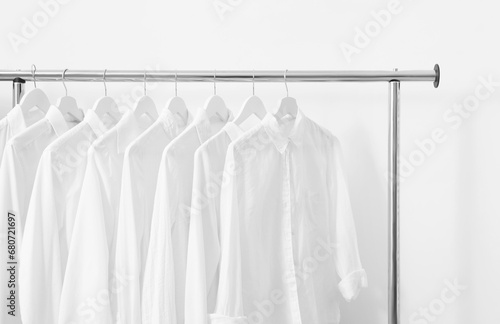 Rack with different stylish shirts near white wall. Organizing clothes © New Africa