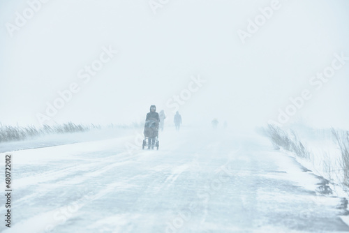 A snowstorm. People walk down the street during a snowstorm. Heavy snowfall. against the background of a cold urban landscape. © justoomm