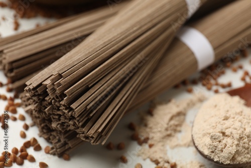 Uncooked buckwheat noodles (soba), flour and grains on white table, closeup
