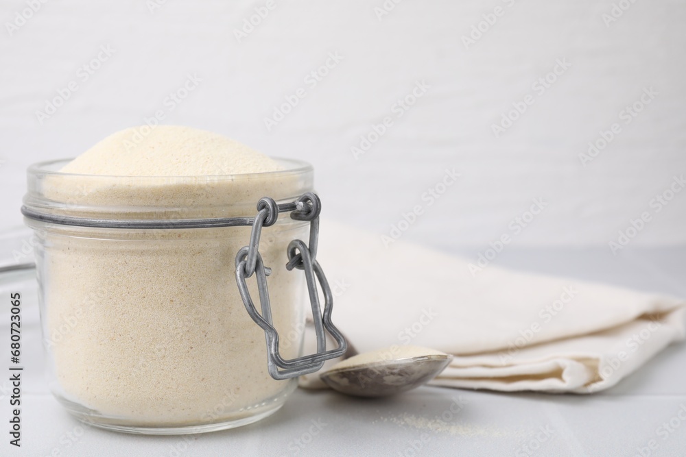 Uncooked organic semolina in jar and spoon on white tiled table, closeup. Space for text Uncooked organic semolina in jar and spoon on white tiled table, closeup. Space for text