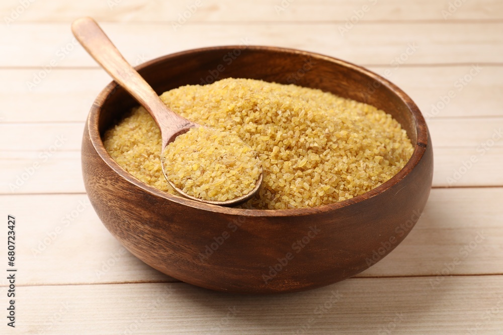 Bowl and spoon with raw bulgur on light wooden table Bowl and spoon with raw bulgur on light wooden table
