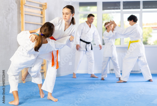 Two girls in kimonos train judo techniques in group in studio