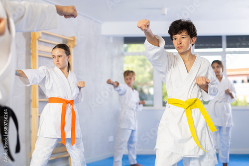 Group of preteen children in kimono trying new martial moves at karate class