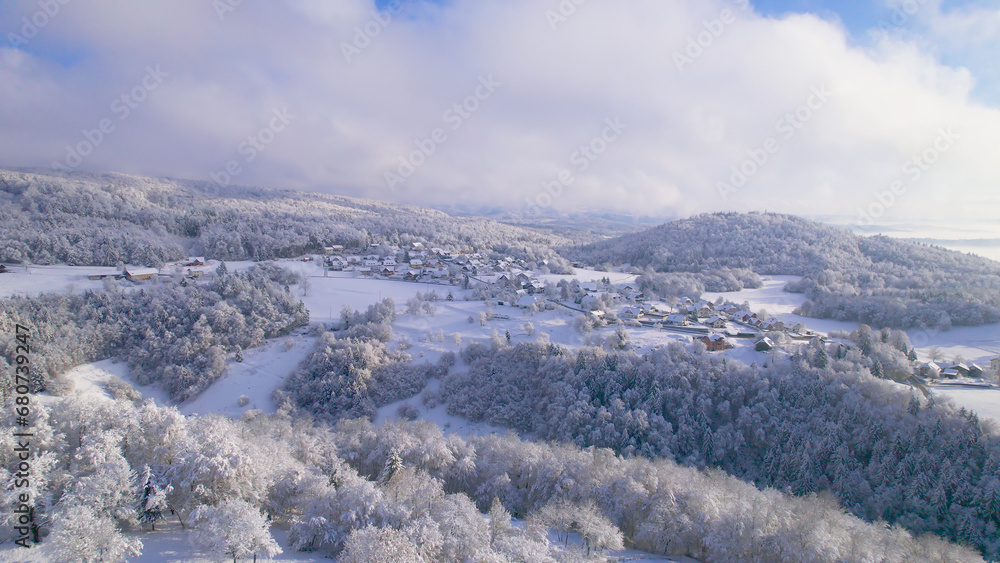 AERIAL: A cute little village on a hill covered with a fresh winter blanket