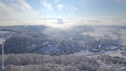 AERIAL  Charming village covered with fresh snow revealing under misty clouds