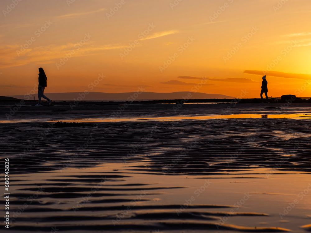 Silhouette of a teenager girl with long hair against sunset sky walking at a beach. Warm orange color. Enjoy outdoor concept. Beautiful nature scene at sunset.