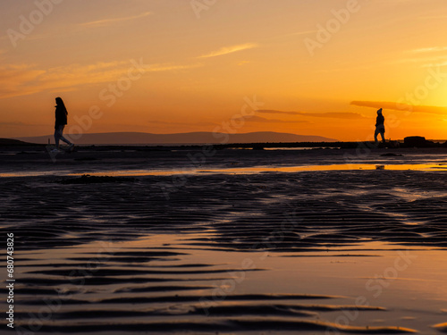 Silhouette of a teenager girl with long hair against sunset sky walking at a beach. Warm orange color. Enjoy outdoor concept. Beautiful nature scene at sunset.