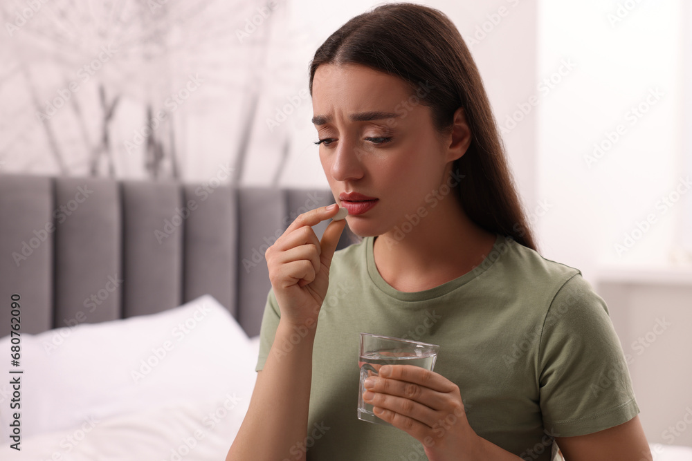 Depressed woman with glass of water taking antidepressant pill on bed indoors, space for text Depressed woman with glass of water taking antidepressant pill on bed indoors, space for text