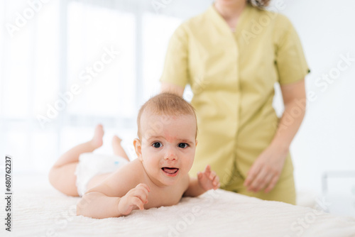 Portrait of cute newborn baby having back massage lying on stomach from professional female masseuse. Cropped shot of therapist young woman therapist performing massage, developing muscles.